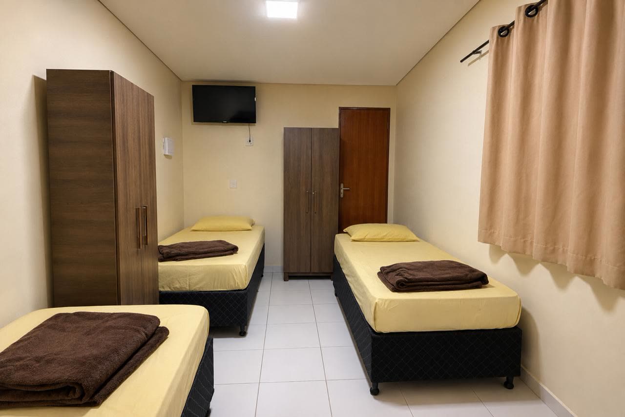 Quarto triplo do Hotel Ideal 2 com três camas de solteiro, guarda-roupas e TV